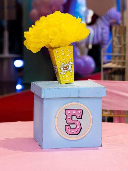 A close-up of a carnival-themed table centerpiece, featuring a popcorn box design and the birthday number.