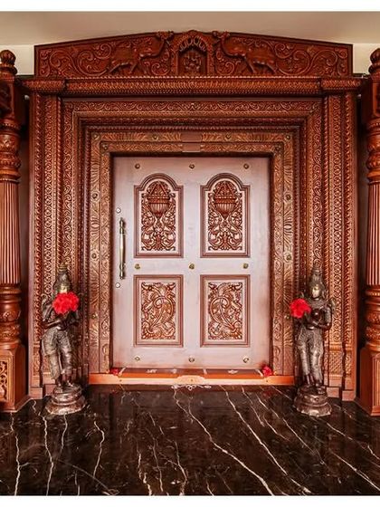 The main puja room door, flanked by marble elephants, features a solid teak wood frame with intricate carvings, creating a sanctified and grand entrance.