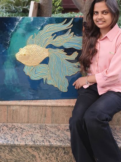 A student proudly displays the textured fish wall art she created in my professional workshop. The piece uses cone art and gold foil to create a stunning 3D effect on a resin background.
