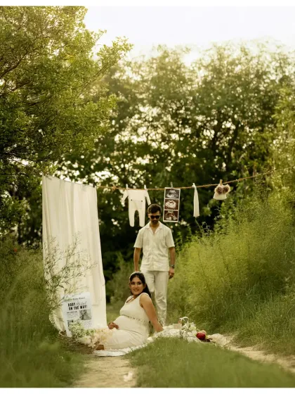 A playful and loving moment captured during their outdoor picnic-themed shoot. The father-to-be stands behind his seated partner, both sharing a happy, relaxed moment.