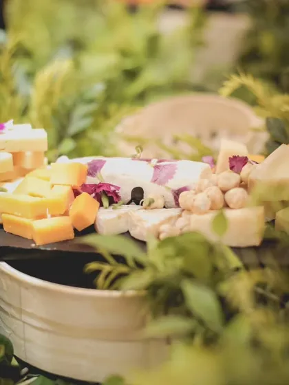 A lush and rustic cheese board, beautifully arranged with various artisanal cheeses and edible flowers amidst fresh greenery. This display is a testament to our commitment to culinary excellence.