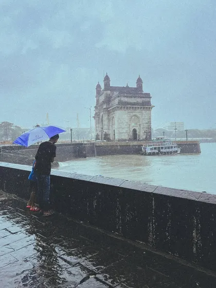 A couple huddles under an umbrella, looking out at the Gateway of India during a downpour. It's a timeless, romantic image that I love to capture.