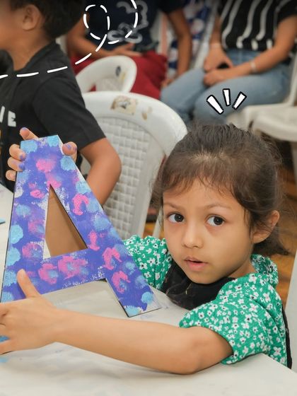A young artist proudly holds up the colorful initial she painted. Personalized crafts like this are a fantastic party activity and a great keepsake for kids to take home.