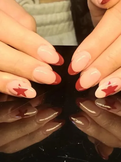 A bold French manicure with deep red tips and a red star accent on a sheer nude base.