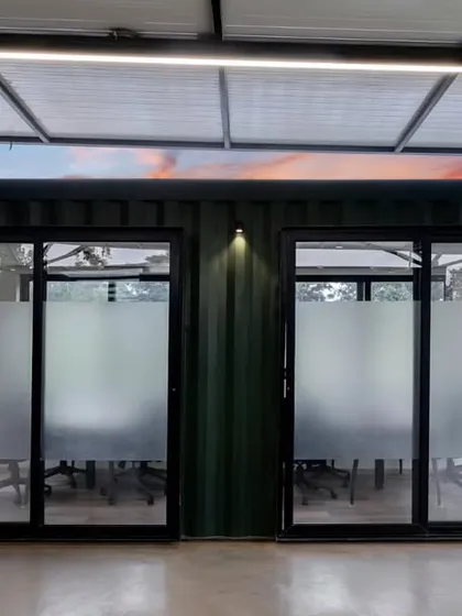 Two private meeting rooms within the container office, viewed from the central courtyard. The frosted glass doors provide privacy while allowing natural light to filter through.