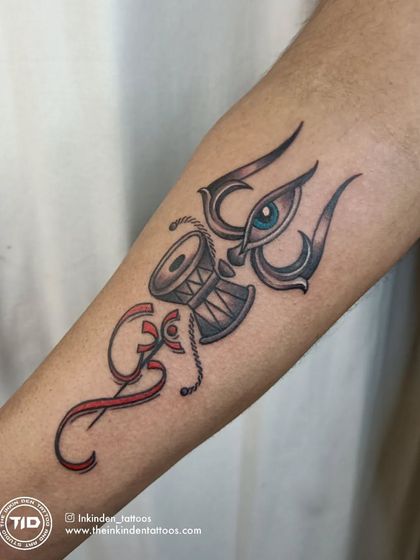A unique composition featuring the Trishul, Damru, and the third eye, combined with the Om symbol. The red accents create a striking contrast and add a layer of energy to this spiritual forearm tattoo.