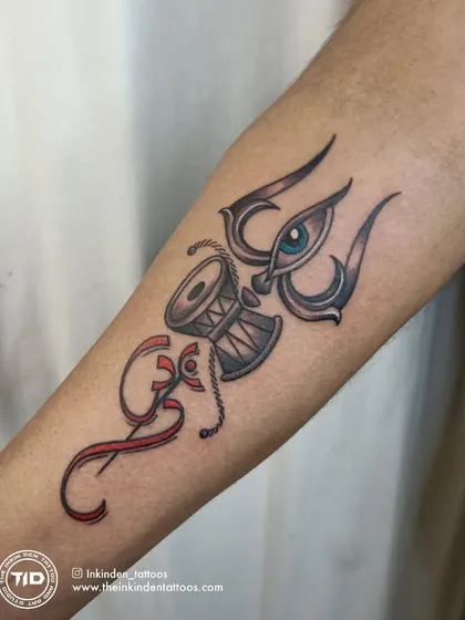 A unique composition featuring the Trishul, Damru, and the third eye, combined with the Om symbol. The red accents create a striking contrast and add a layer of energy to this spiritual forearm tattoo.