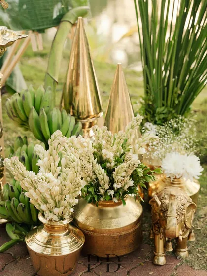 A collection of traditional decor items, including brass pots, a brass elephant, and fresh tuberose, creating a rich and auspicious display.