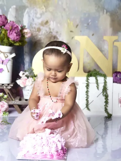 A classic first birthday cake smash moment. Dressed in a beautiful pink gown, this little one is enjoying her very first taste of birthday cake in a lovely floral garden setting.