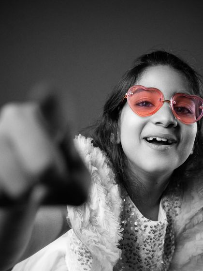 I love how this shot captures so much personality. The selective color technique highlights her fun, heart-shaped glasses while the rest of the image is in black and white. Her expressive face and pose make this a truly dynamic and engaging portrait.