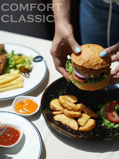 A satisfying two-handed grip on my gourmet burger, served on a black plate with seasoned potato wedges and a fresh side salad.