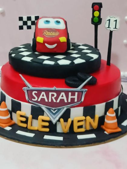 A "Cars" themed cake for an eleventh birthday. This two-tiered cake features a race track, traffic signs, and a Lightning McQueen topper.