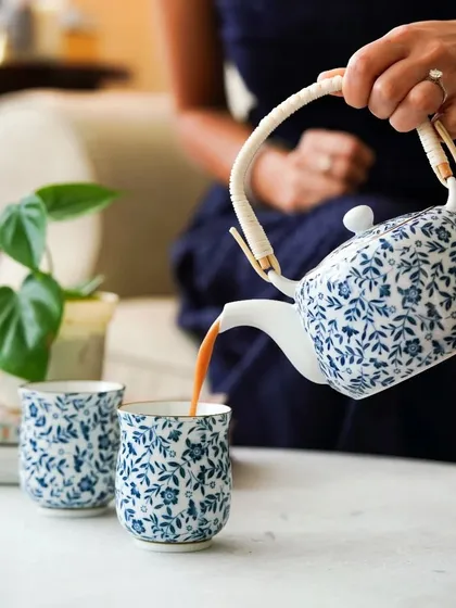 A woman pouring tea from a beautiful blue and white ceramic teapot, a classic and elegant lifestyle shot.