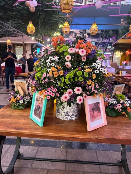 A beautiful floral centerpiece on a rustic wooden table, with framed baby photos adding a personal touch to this Bridgerton-inspired Godh Bharai.