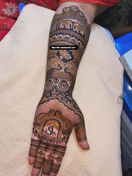 The back of the arm of a bridal design, featuring the couple's initial "S" and traditional elephant and peacock figures.