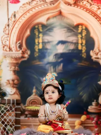 A full view of our Krishna setup, showing the baby sitting amidst a grand backdrop with ornate pillars and peacock decor.