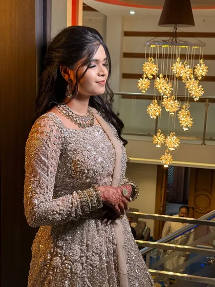 A bride in a shimmering silver Anarkali, looking elegant under a chandelier.