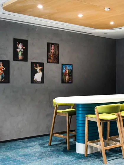 A collaborative space in The Citco Group's office, featuring a high table with bright green stools. The wall is decorated with framed art depicting traditional Indian dance forms, blending corporate design with local culture.