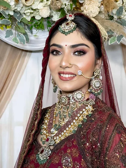 This bride’s smile says it all. Her makeup is fresh and radiant, with a focus on bright eyes and a flawless complexion that looks stunning against her maroon bridal wear.