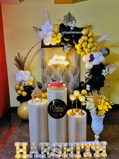 A rustic-chic birthday decor with a black and yellow balloon arrangement. The setup includes a custom backdrop, neon sign, and dried floral elements.