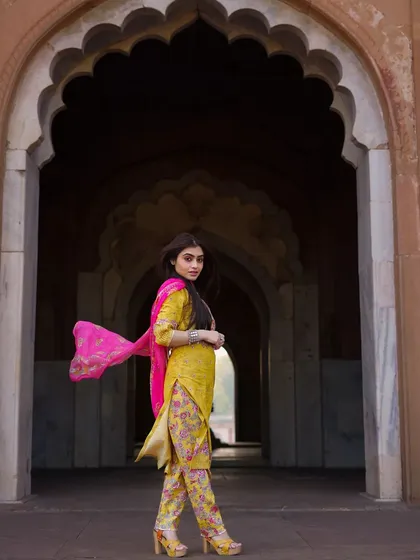 A candid moment of movement within the archway. The flowing dupatta adds a sense of grace and motion, bringing the entire outfit to life in this ethnic fashion portrait.