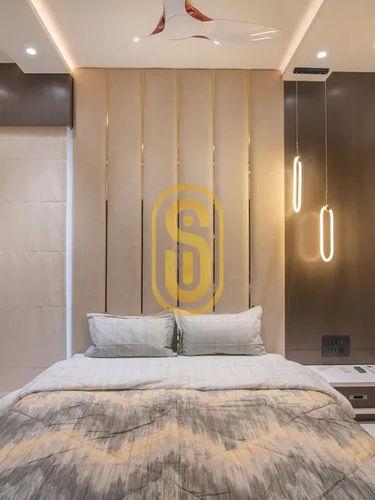 An elegant bedroom featuring a floor-to-ceiling upholstered headboard with vertical brass inlays. The modern pendant lights on either side of the bed serve as both functional reading lights and stylish decor.