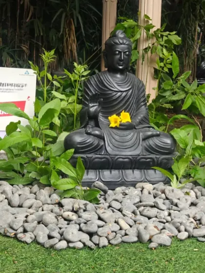 The serene expression of the hand-carved Buddha statue brings a sense of calm to the space. The addition of fresh yellow flowers is a simple touch that enhances its spiritual feel.