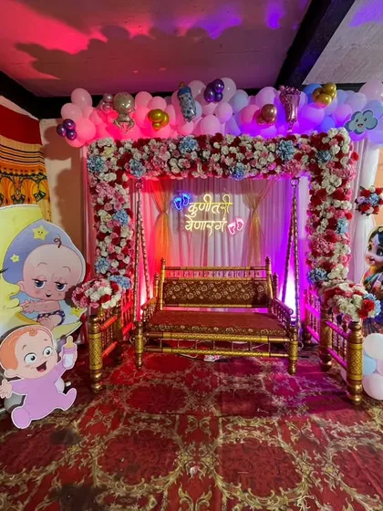 A traditional godh bharai setup with a decorated swing, framed by a floral and balloon arch. The theme includes baby character cutouts and a crescent moon prop.