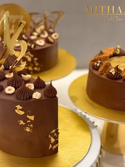 A trio of my signature chocolate cakes. Each one is uniquely decorated with elements like hazelnuts, gold leaf, custom initial toppers, and butterfly accents, showcasing the versatility of a classic chocolate cake.
