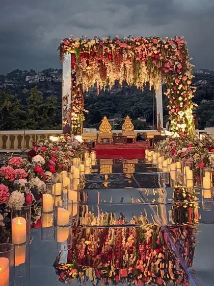 A mandap with a view. Set against the magnificent backdrop of the Mussoorie hills, this mirrored mandap is framed by a lush arch of colorful blooms and a candle-lit aisle, creating a breathtaking fusion of natural and designed beauty.