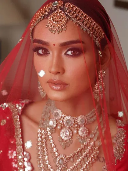 A close-up of a classic red bridal look. The focus is on the eyes, with a sharp wing and soft smoke, paired with a perfectly defined lip. The skin is kept fresh to balance the richness of the attire.