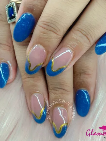 A royal combination of deep blue and gold. This design features sparkling blue glitter nails and accent nails with a modern, wavy French tip outlined in gold.