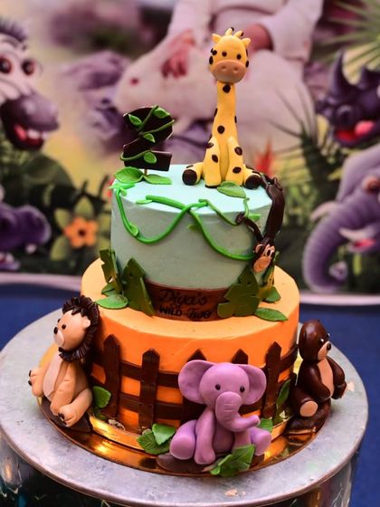 The cake for the jungle-themed birthday party. It's a two-tiered cake decorated with fondant animals like a giraffe, lion, and elephant, matching the backdrop perfectly.