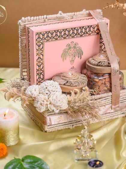 A beautiful Karwa Chauth hamper featuring a pink sweet box and premium nuts, all arranged in a rustic woven basket with elegant floral details.