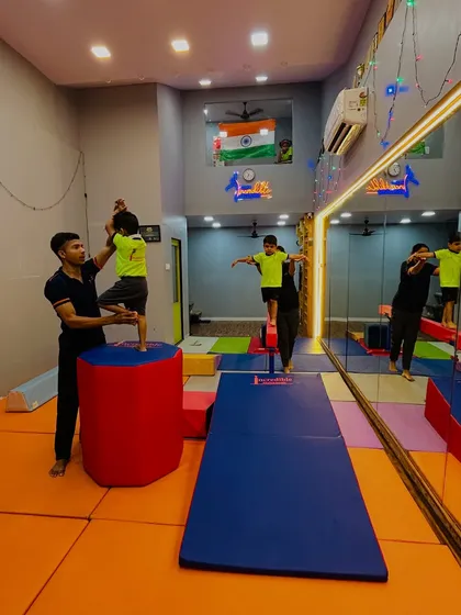 We give special attention to our littlest gymnasts. Here, an instructor helps a toddler with a balance exercise on a soft, cylindrical tumbler, showing how we make learning safe and engaging for even the youngest children.