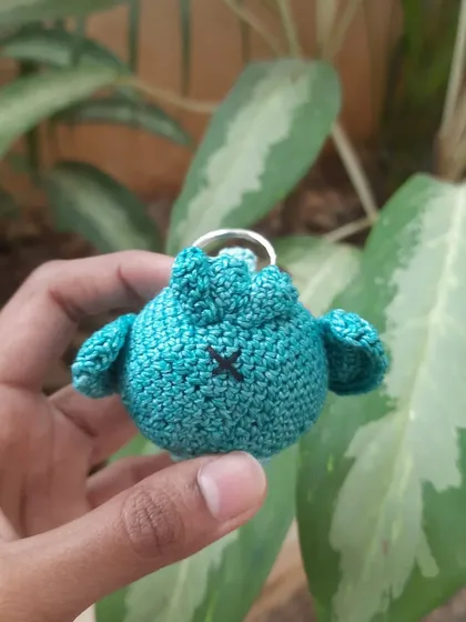 The back of the little blue amigurumi, showing the 'x' detail that gives it a handmade, rustic charm.