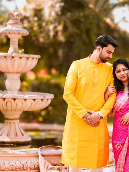 A romantic pose by a classic water fountain. The groom's bright yellow kurta and the bride's pink bandhani saree create a beautiful color combination.