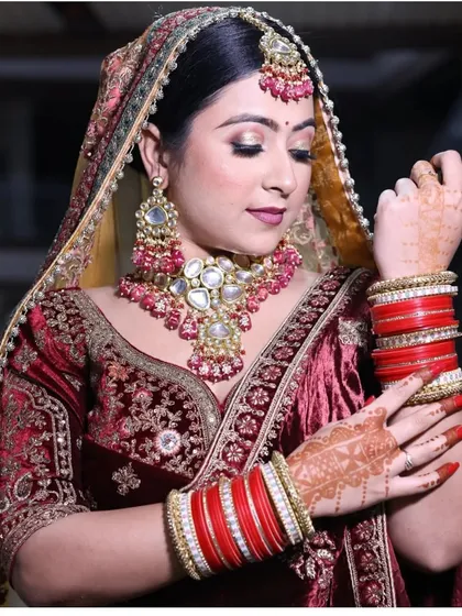 A beautiful shot focusing on the bride's hands, adorned with henna and traditional red and gold bangles, complementing her embroidered maroon velvet lehenga.
