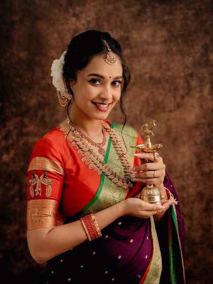A close-up portrait focusing on traditional details. The mom-to-be holds a brass lamp (diya), symbolizing light and life, complementing her beautiful saree and jewelry.