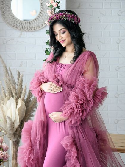 A close-up solo portrait highlighting the beautiful details of the dusty rose ruffled gown and the mom-to-be's serene expression. The boho backdrop adds a touch of warmth.