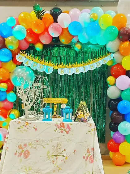 A vibrant, multi-colored balloon arch with a green shimmer backdrop. This versatile setup is perfect for a tropical or jungle-themed party and creates an instant festive mood.
