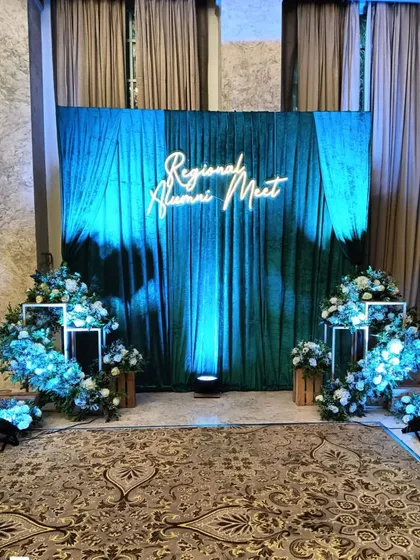 For this regional alumni meet, I designed a sophisticated stage with a rich green velvet curtain and a custom neon sign. The blue uplighting and floral arrangements create a premium and memorable atmosphere for formal gatherings.