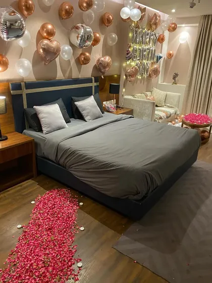 A full view of a sophisticated birthday room makeover. This angle shows the path of red rose petals on the floor, leading towards the decorated bed and a side table also covered in petals, tying the whole romantic theme together.