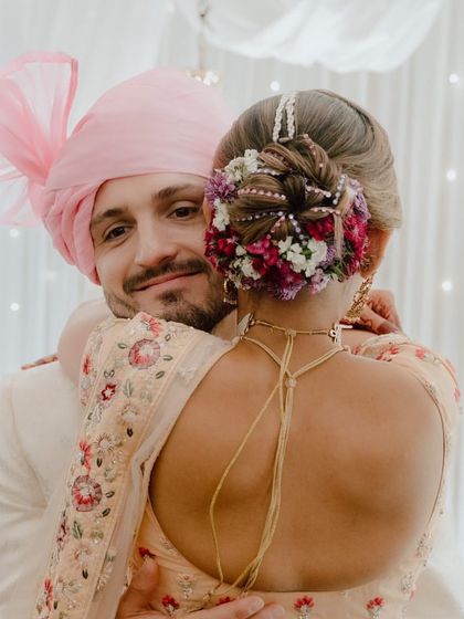 A candid, emotional moment between the bride and groom, with a beautiful view of her intricate floral bun. This is what wedding memories are made of.