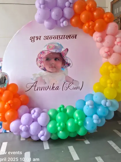 A colorful and personal setup for a traditional Annaprashan ceremony. This features a custom backdrop with the baby's photo and name, framed by a vibrant rainbow balloon arch.