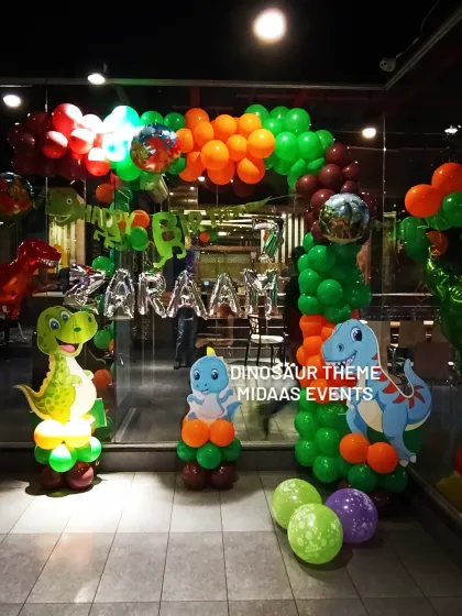 A vibrant dinosaur-themed balloon entrance with character cutouts and foil name balloons for Zaraah's party.