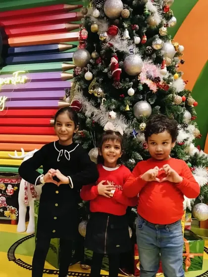 Three friends make heart shapes with their hands in front of our festive Christmas tree.