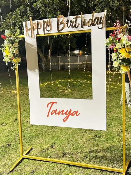 A personalized 'Happy Birthday' photo frame for guests to take pictures, set up in the garden area with fairy lights in the background.