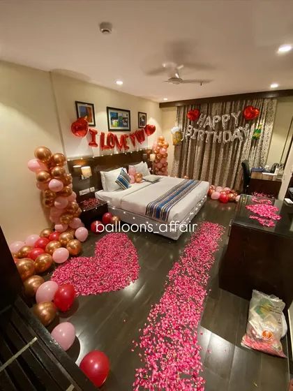 A wide angle of the hotel room decoration, showing the large heart shape made of rose petals on the floor and the pathway leading to the bed.