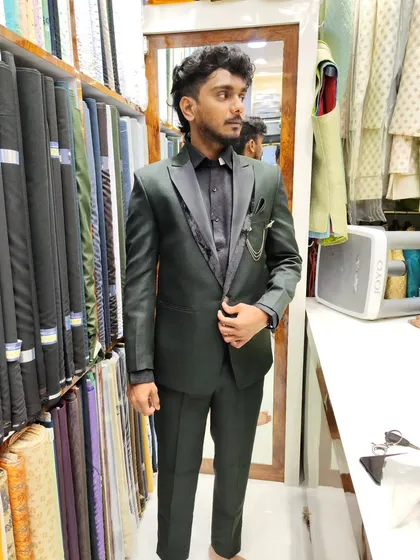 A client modeling a sleek designer suit in a deep bottle green. This two-piece suit with a contrasting black shirt is a modern and stylish option for any wedding event.